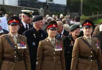 Three female soldiers stand in brown ceremonial uniforms at the start of a parade.