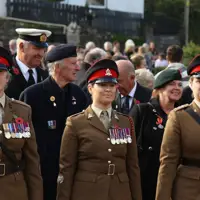 Three female soldiers stand in brown ceremonial uniforms at the start of a parade.