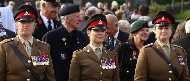 Three female soldiers stand in brown ceremonial uniforms at the start of a parade.