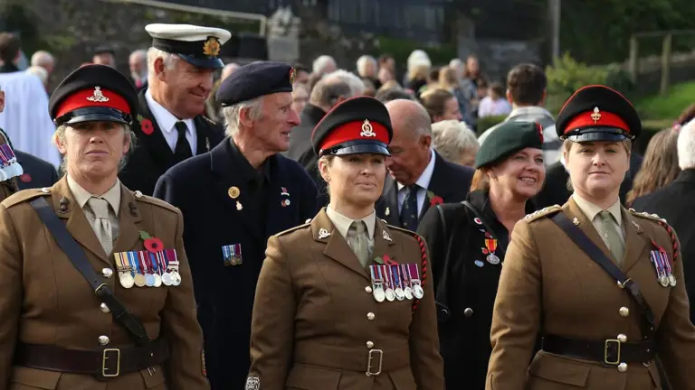 Three female soldiers stand in brown ceremonial uniforms at the start of a parade.