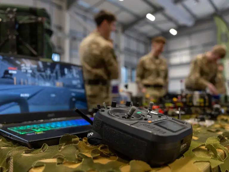 Military drone controller and laptop with simulation software on a camouflaged table inside a training facility.