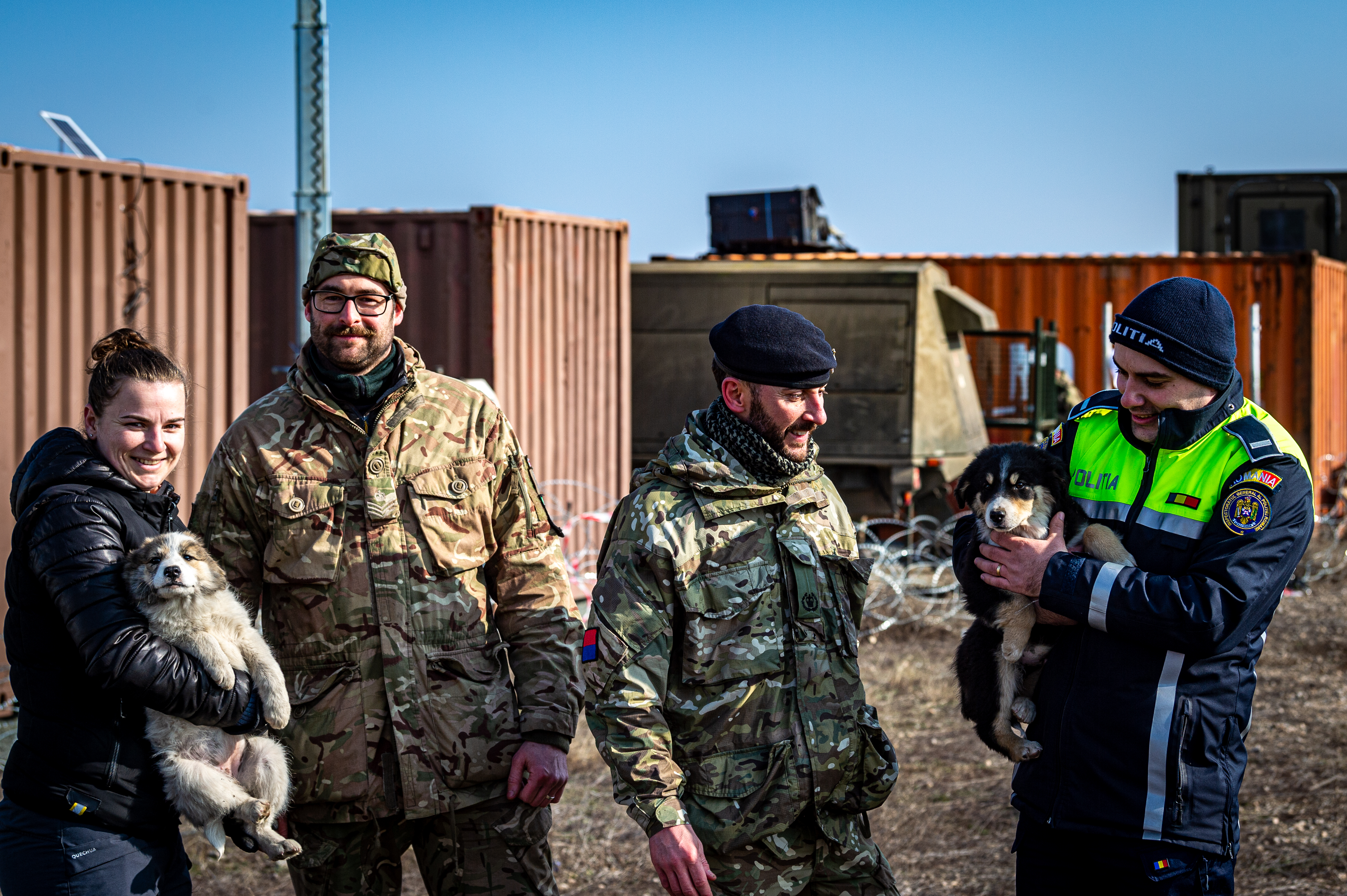 Two personnel in uniform are stood with people holding puppies on either side, the lady on the left is dressed in civilian attire and the man on the right is in police uniform.