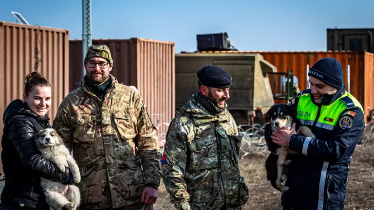 Two personnel in uniform are stood with people holding puppies on either side, the lady on the left is dressed in civilian attire and the man on the right is in police uniform.
