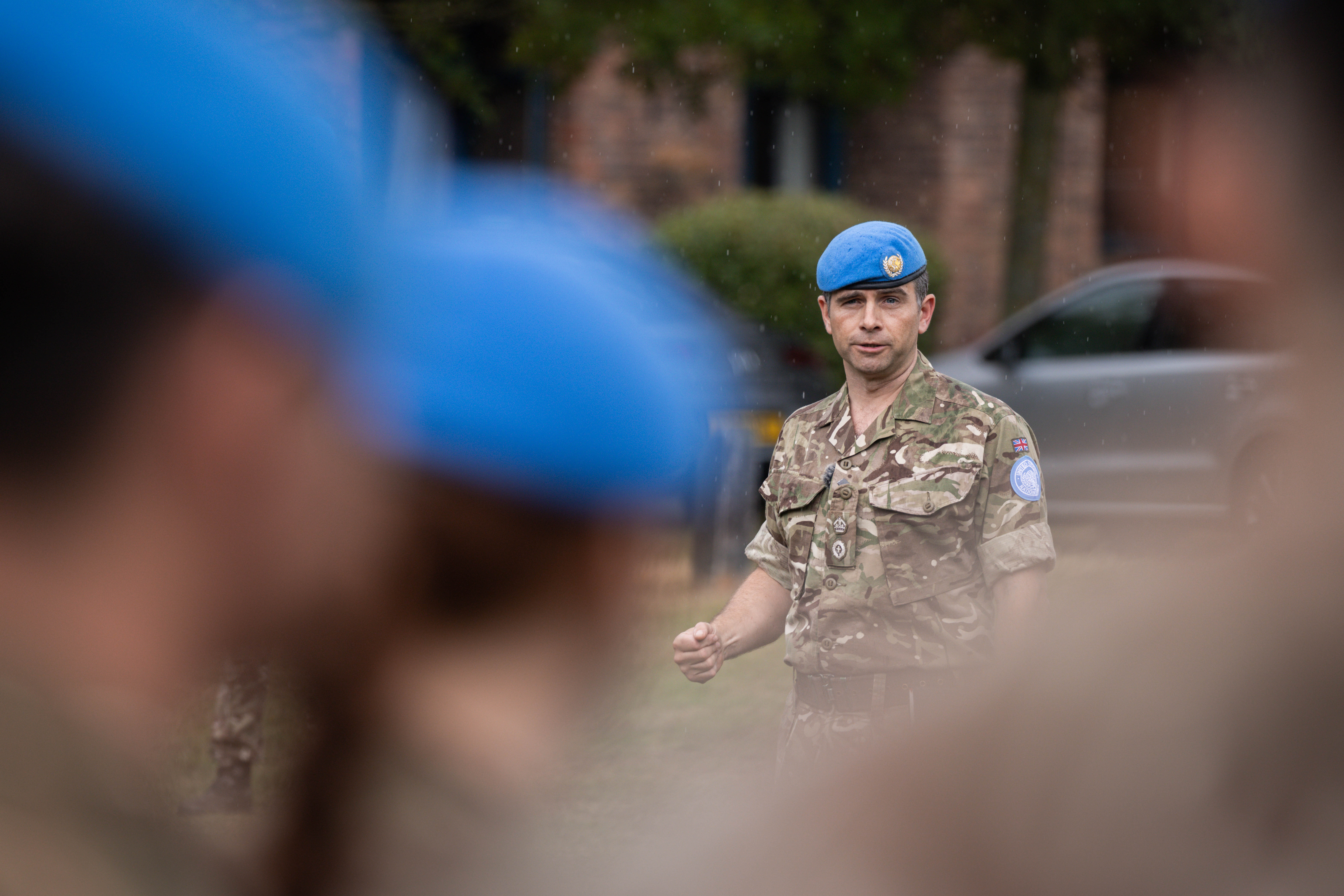 A soldier in camouflage uniform with a blue beret on his head talks to his soldiers.