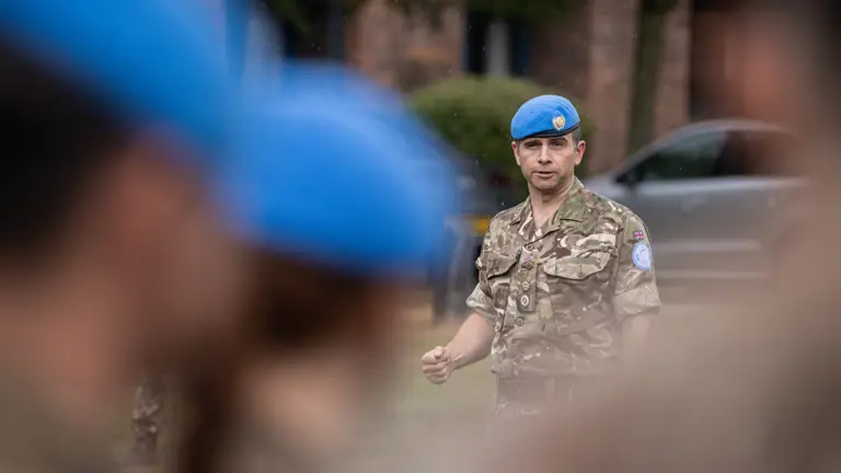 A soldier in camouflage uniform with a blue beret on his head talks to his soldiers.