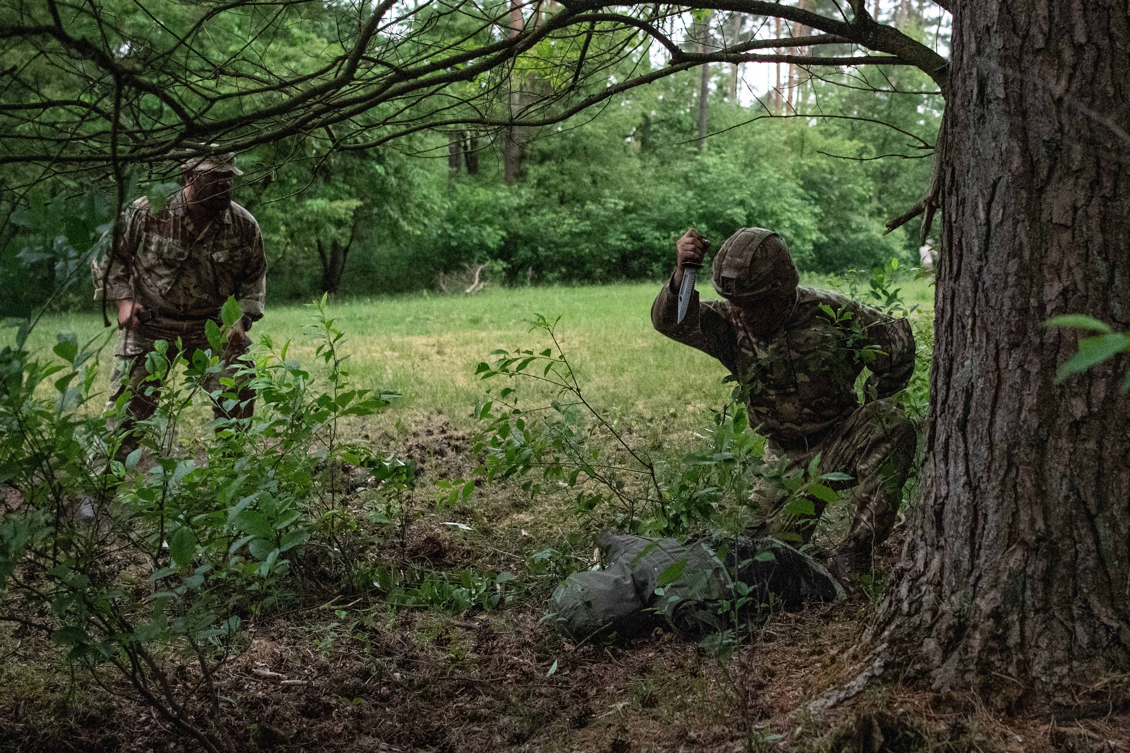 Officer Cadets wearing camouflaged uniform conducting bayonet drills with a Socket Bayonet underneath tree growth.
