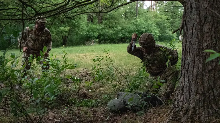 Officer Cadets wearing camouflaged uniform conducting bayonet drills with a Socket Bayonet underneath tree growth.