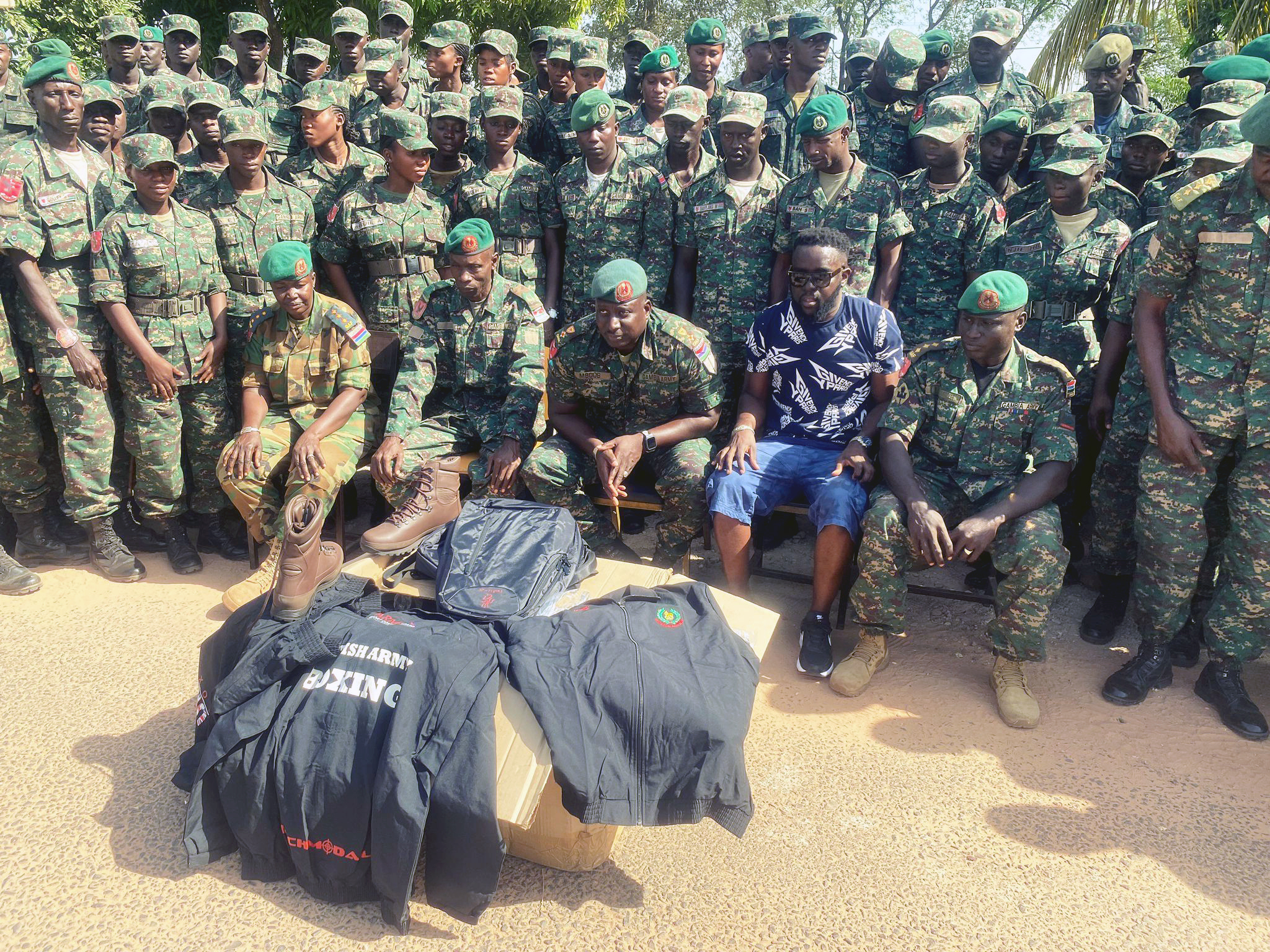 Group of soldiers in camouflage uniforms and green berets posing outdoors with military gear.