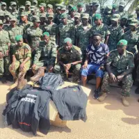 Group of soldiers in camouflage uniforms and green berets posing outdoors with military gear.