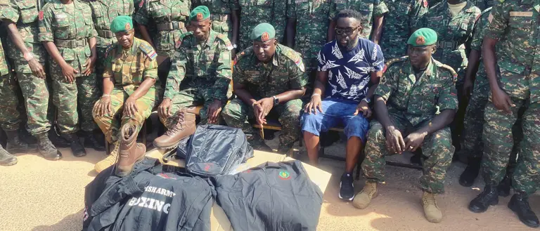 Group of soldiers in camouflage uniforms and green berets posing outdoors with military gear.