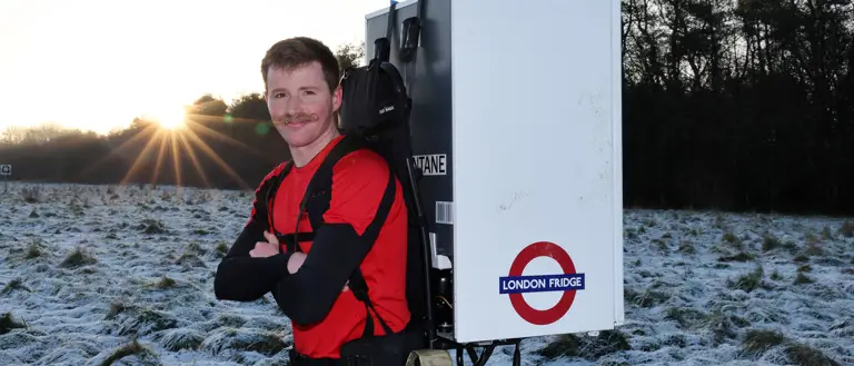 Major Joss Mowforth, pictured in his workout clothes posing for a portrait outside in snowy weather carrying a fridge strapped to his back.