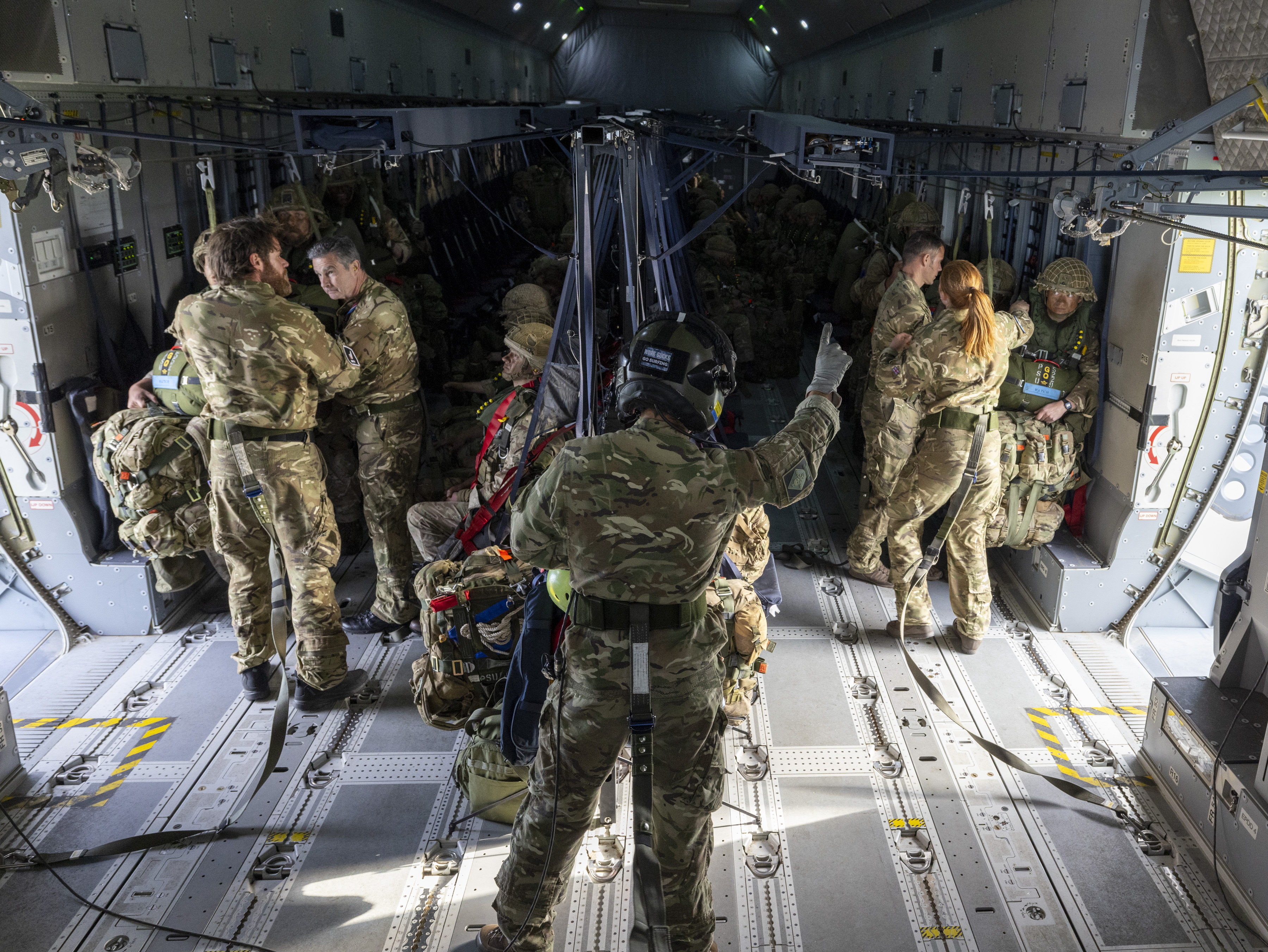 Soldiers in camouflage gear prepare for a parachute jump inside a military aircraft.
