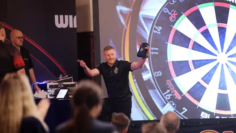 Player celebrating a successful dart throw in front of a large projected dartboard during a tournament.