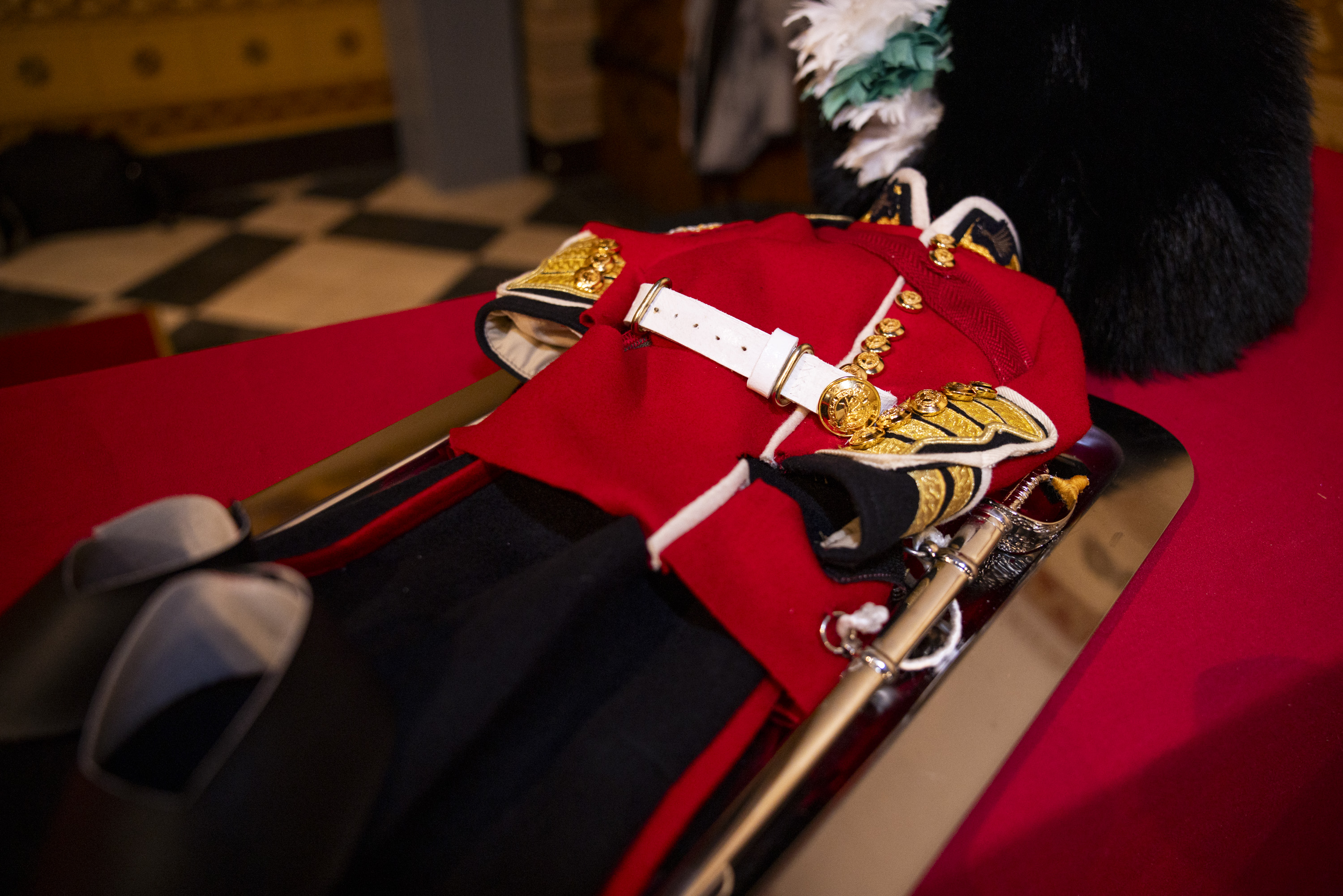 Traditional British red military dress uniform with gold buttons and white belt displayed on a table.