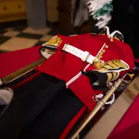 Traditional British red military dress uniform with gold buttons and white belt displayed on a table.