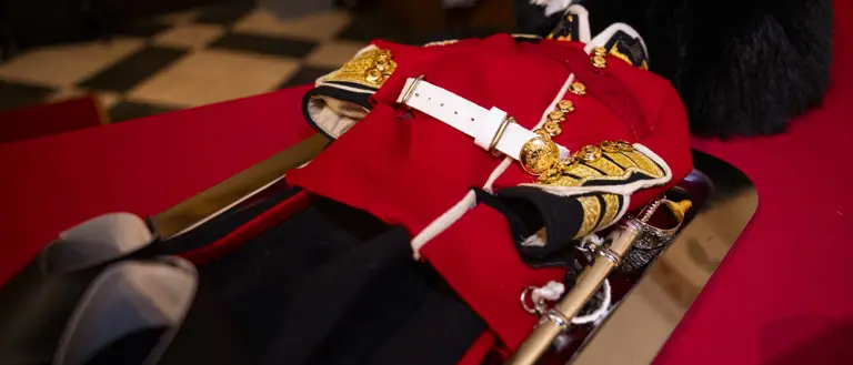 Traditional British red military dress uniform with gold buttons and white belt displayed on a table.