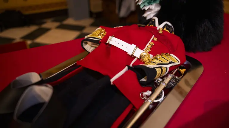 Traditional British red military dress uniform with gold buttons and white belt displayed on a table.