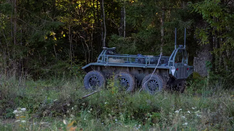 An unmanned resupply vehicle shown in the woodlands completely unmanned and delivering supplies to the soldiers in the woods.