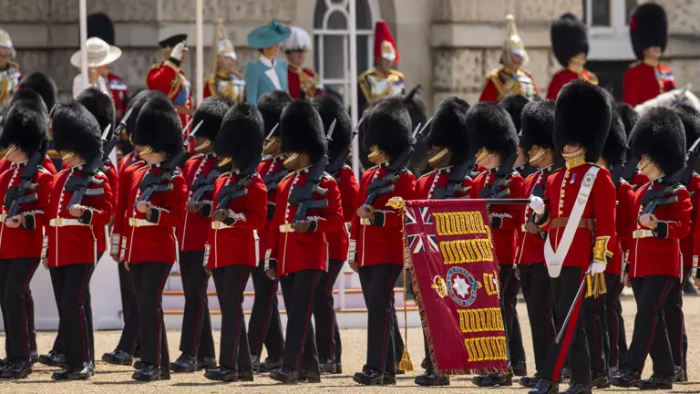 Two lines of soldiers in red tunics and bearskin hats stand with their rifles pointing upwards.