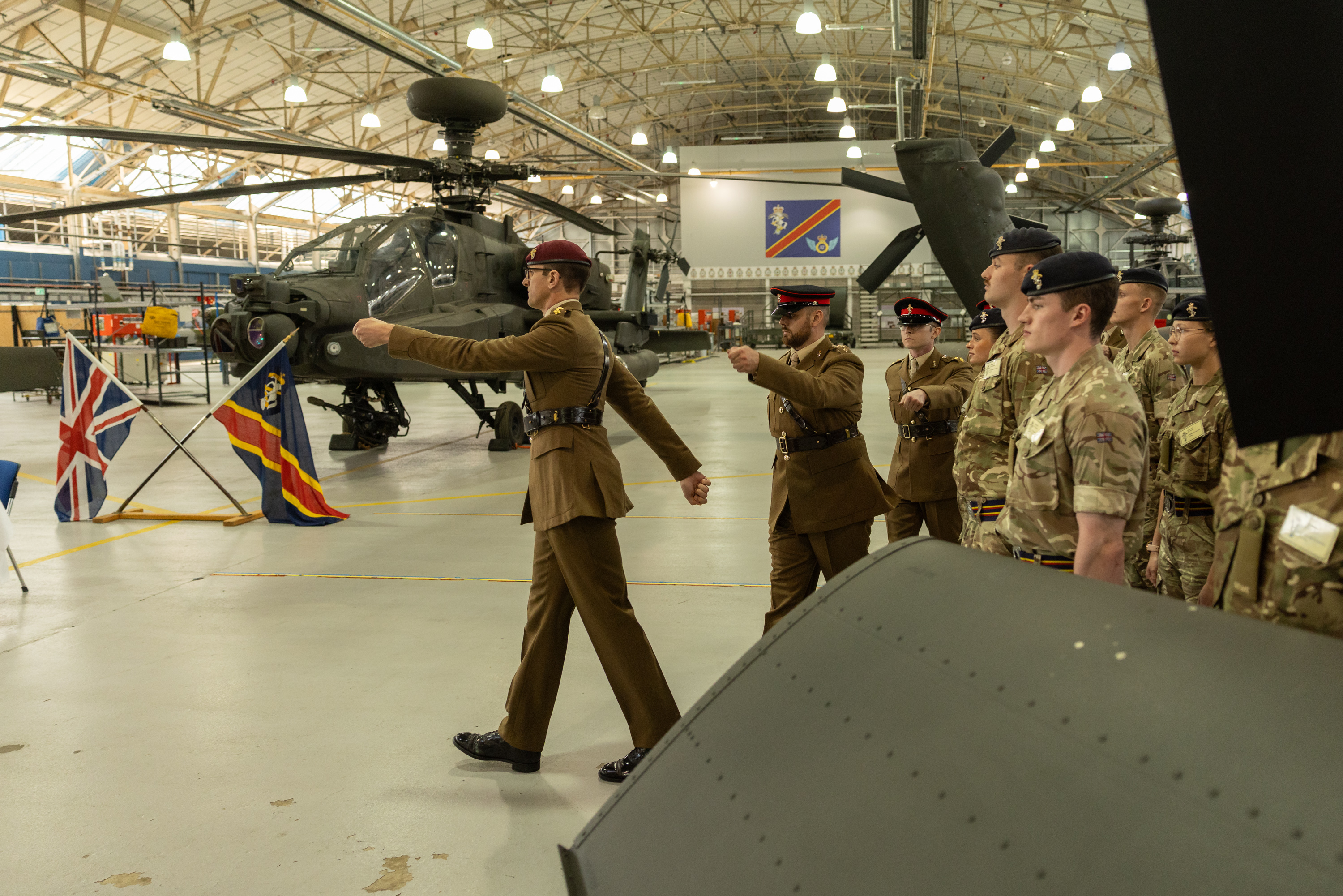 Soldiers in brown ceremonial uniforms march in front of a green military helicopter.
