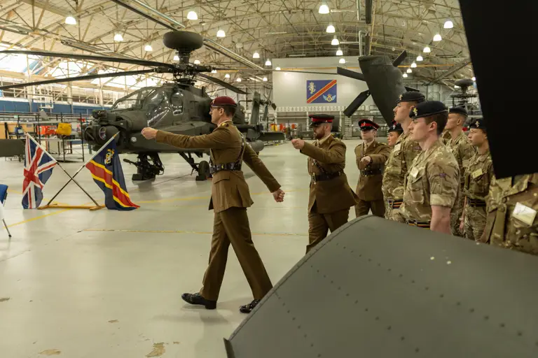 Soldiers in brown ceremonial uniforms march in front of a green military helicopter.