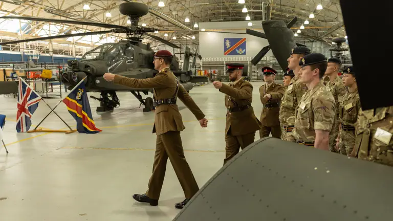 Soldiers in brown ceremonial uniforms march in front of a green military helicopter.