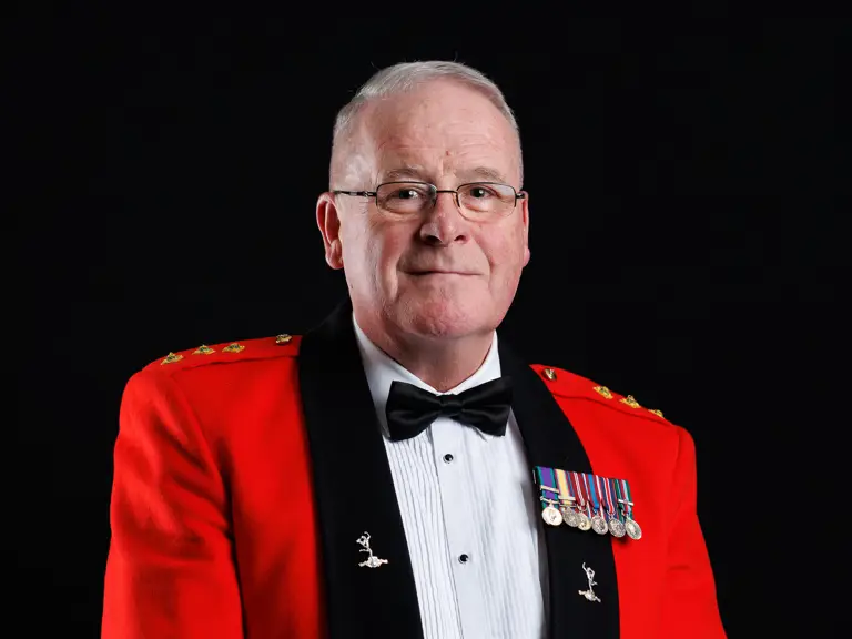 Man in a formal red military dress jacket with medals and a black bow tie holding a conductor's baton.