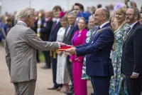 His Majesty The King places his hand onto a red pillow as a crowd looks on.