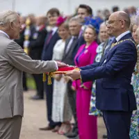 His Majesty The King places his hand onto a red pillow as a crowd looks on.
