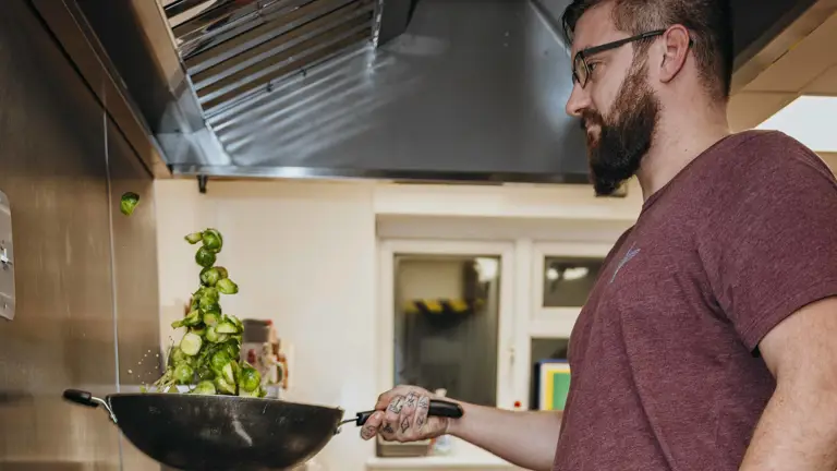 A man in a purple t-shirt and camo trousers prepares brussel sprouts.