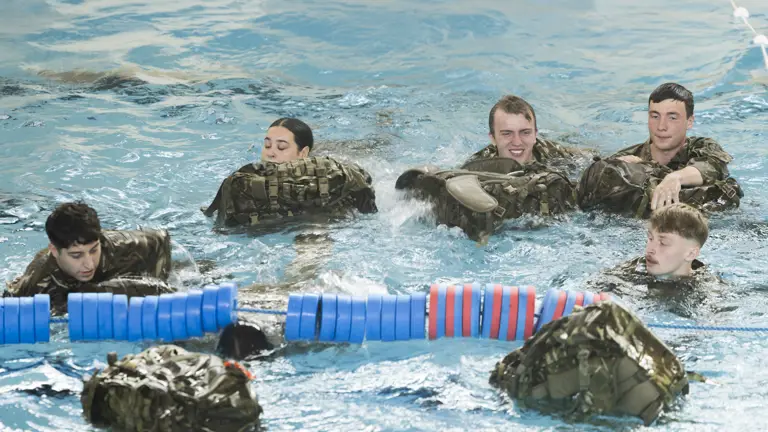 Group of soldiers in camouflage uniforms practicing water survival skills in a pool, partially submerged.