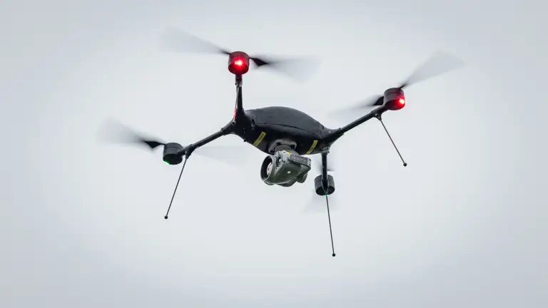 A black drone flies against a grey sky.