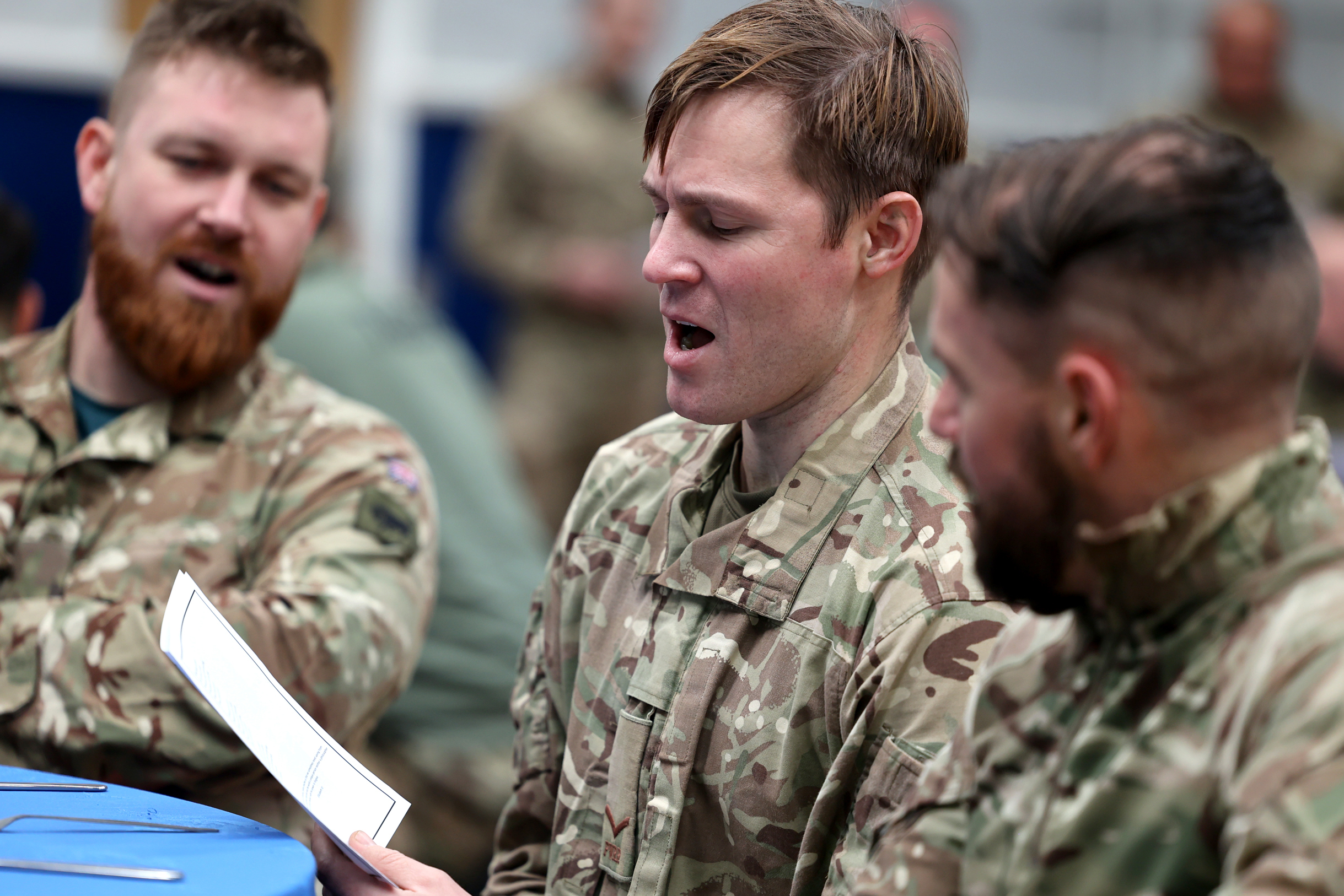 Three soldiers sing Christmas songs from one lyric sheet.