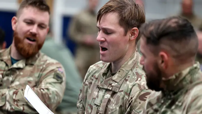 Three soldiers sing Christmas songs from one lyric sheet.