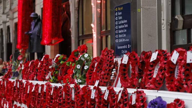 Poppy wreaths are displayed along a wall. A train station sign reads 'Welcome to Paddington Station'.