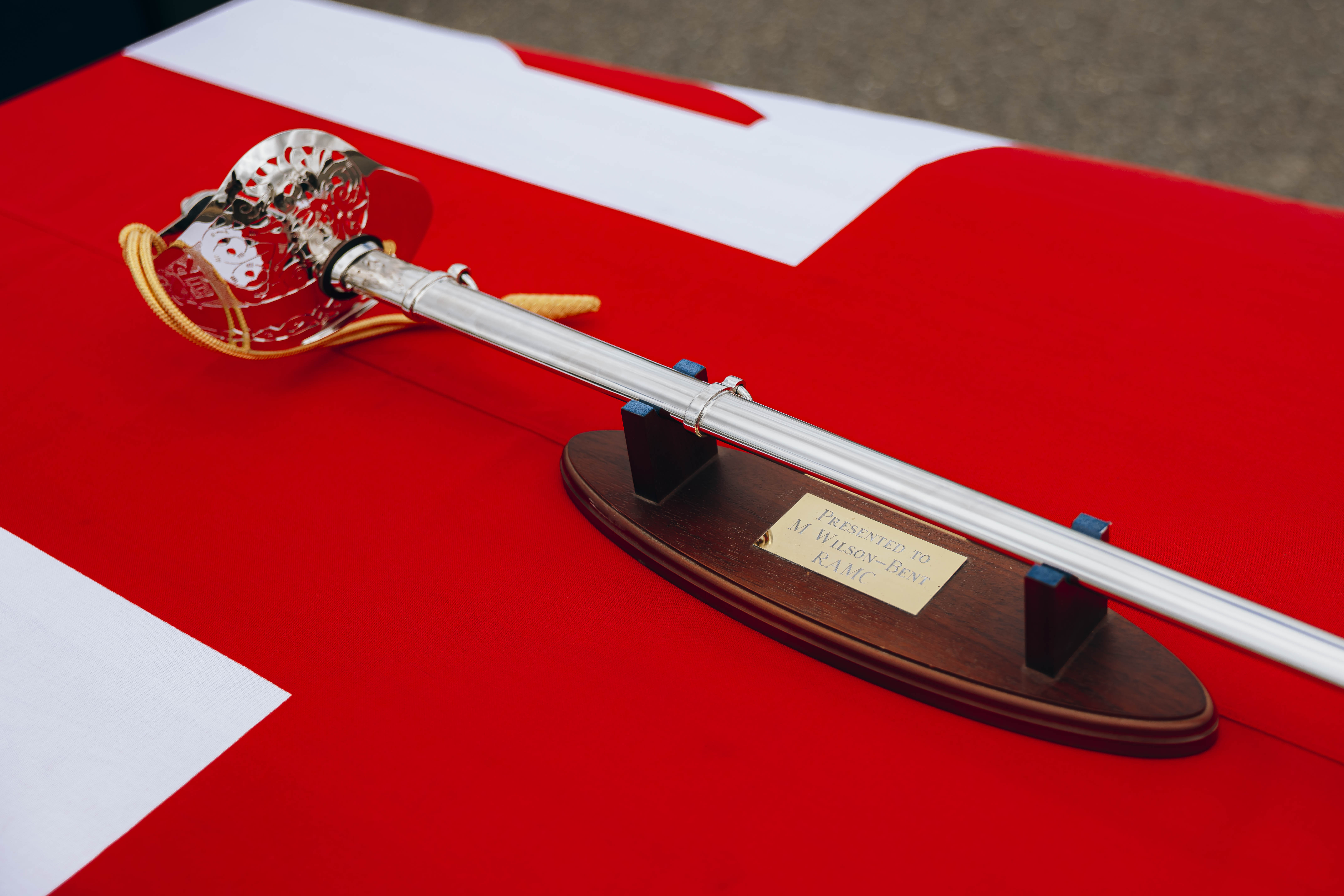 A sword is laid on a table, there is a Union Flag draped on the table underneath the sword.