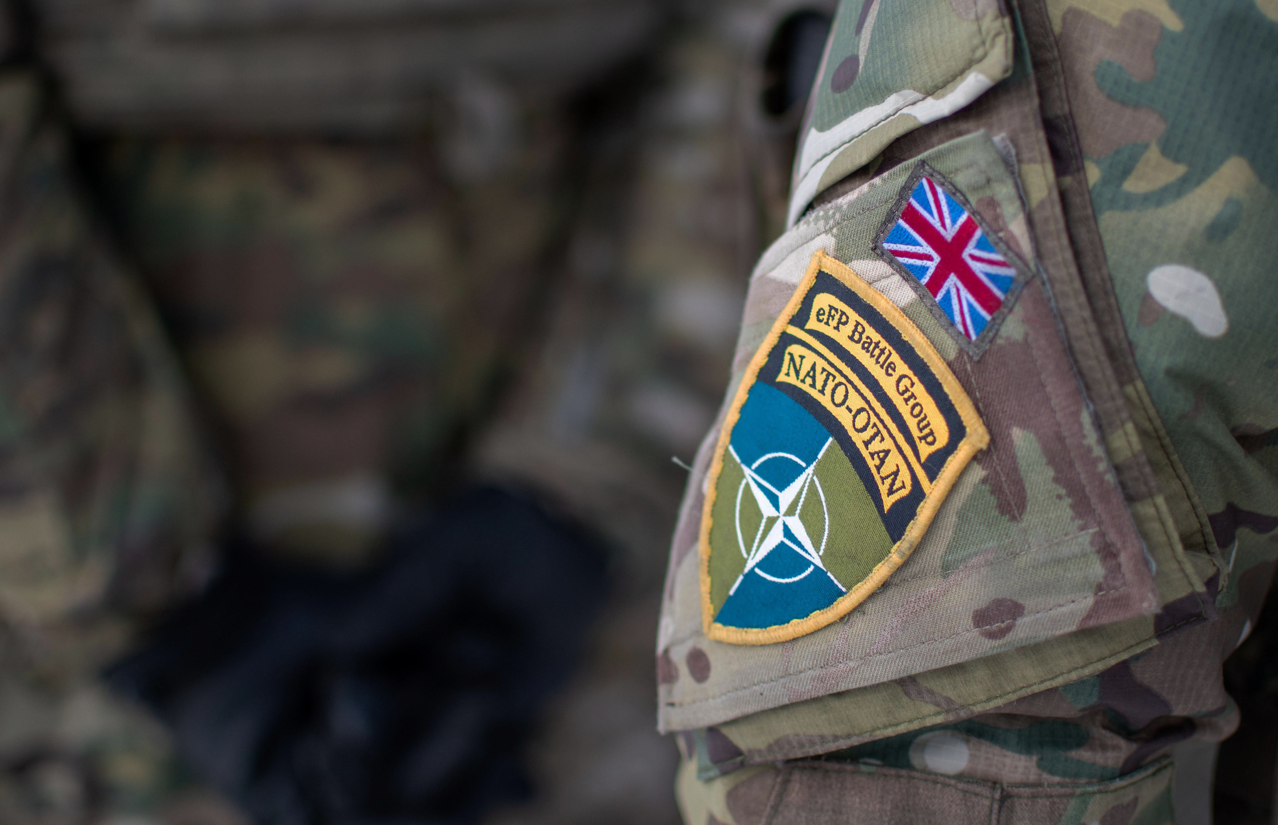 Camouflage uniform close up on the arm. NATO symbolic star shown with the colours green and blue. The Union Jack is placed above this.