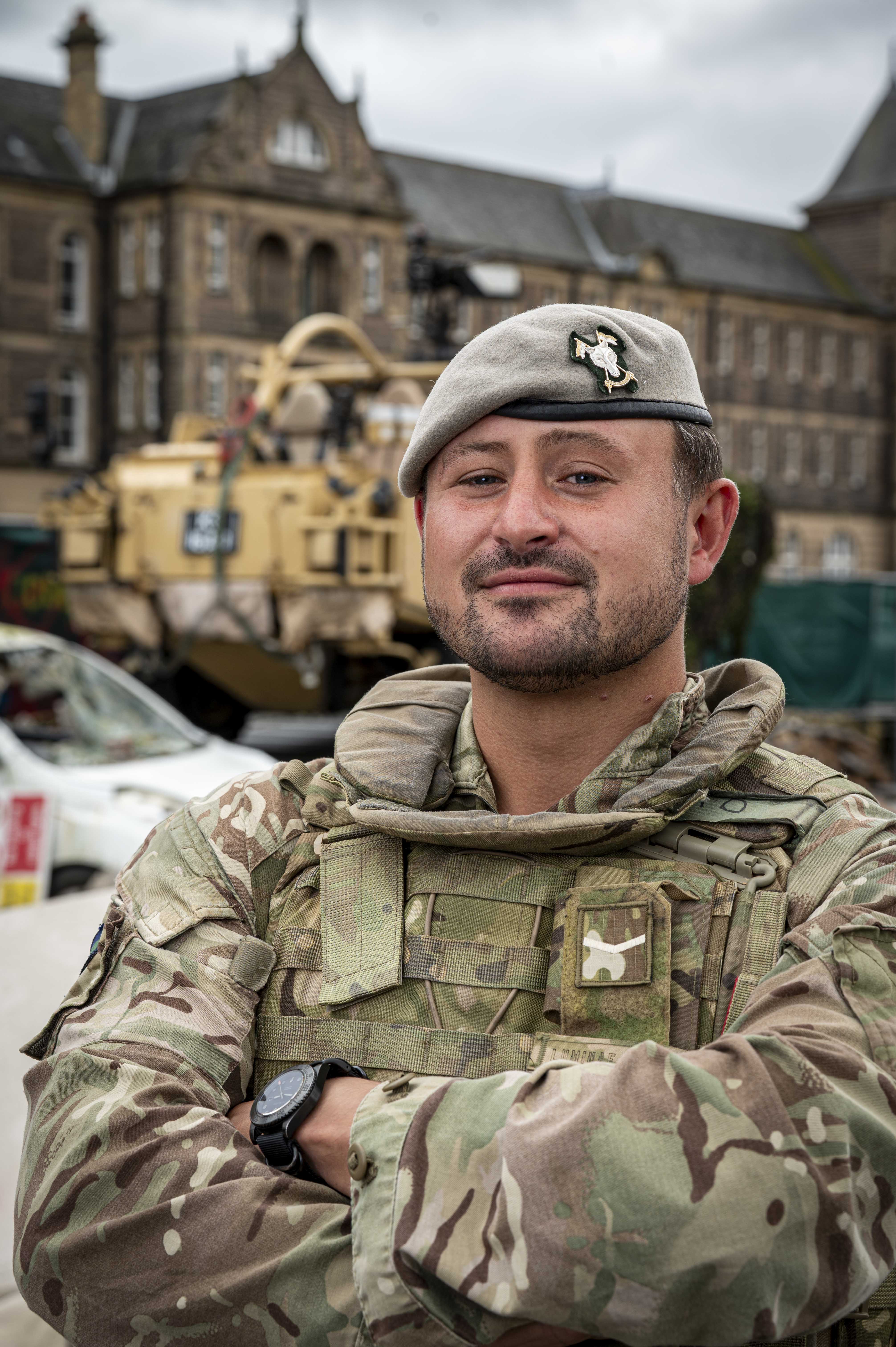 Soldier in camouflage uniform and beret stood posing for a portrait in front of a Jackal Vehicle  