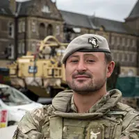 Soldier in camouflage uniform and beret stood posing for a portrait in front of a Jackal Vehicle