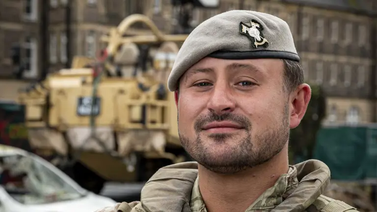 Soldier in camouflage uniform and beret stood posing for a portrait in front of a Jackal Vehicle