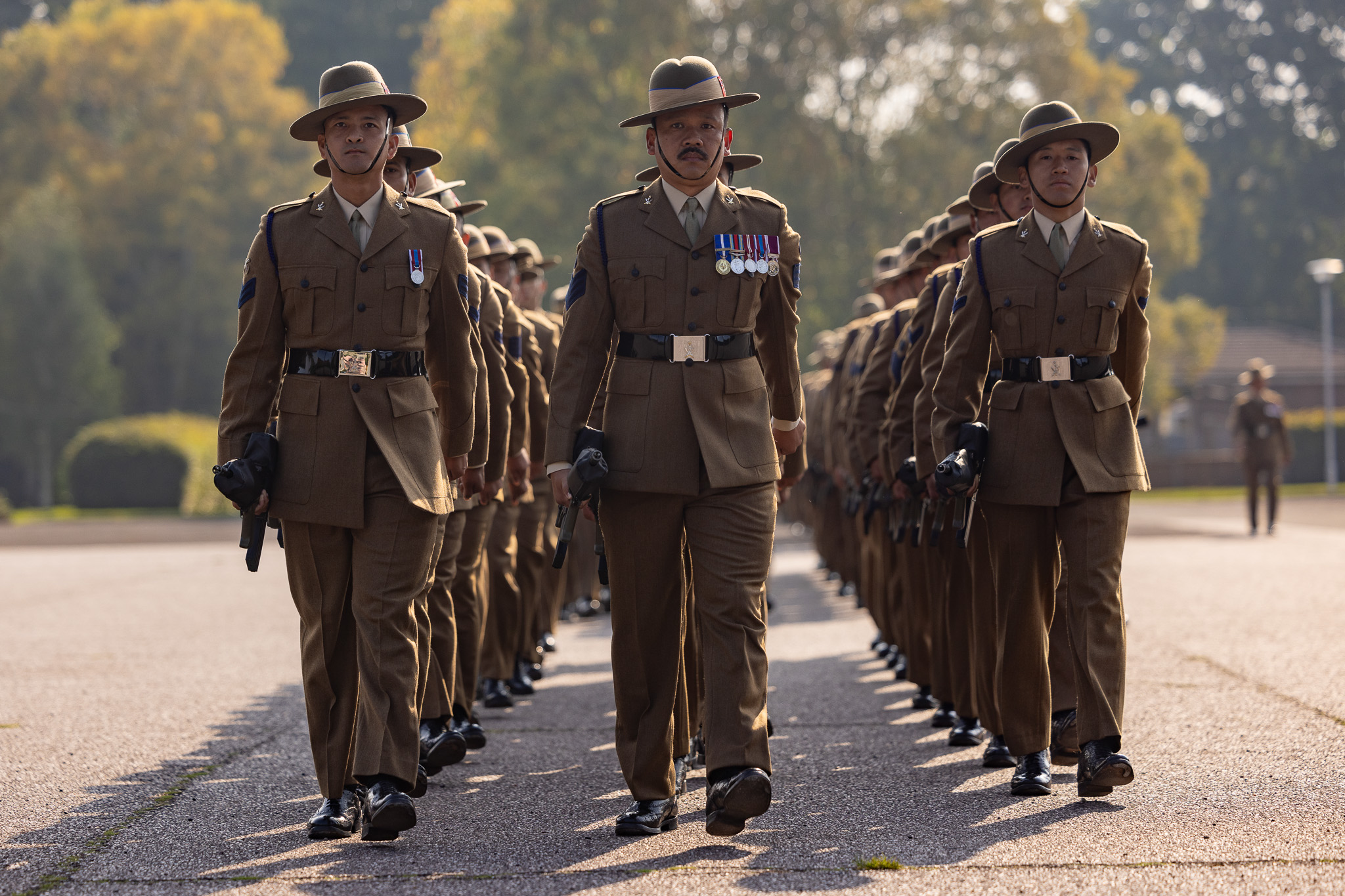 Three lines of soldiers in brown ceremonial uniform are pictured marching. 
