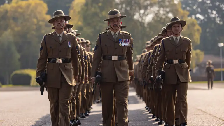 Three lines of soldiers in brown ceremonial uniform are pictured marching.