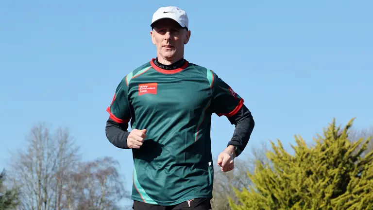 A man in athletic gear runs on an outdoor track under a clear blue sky. Green trees and a fence line the background, conveying a sense of focus and energy.