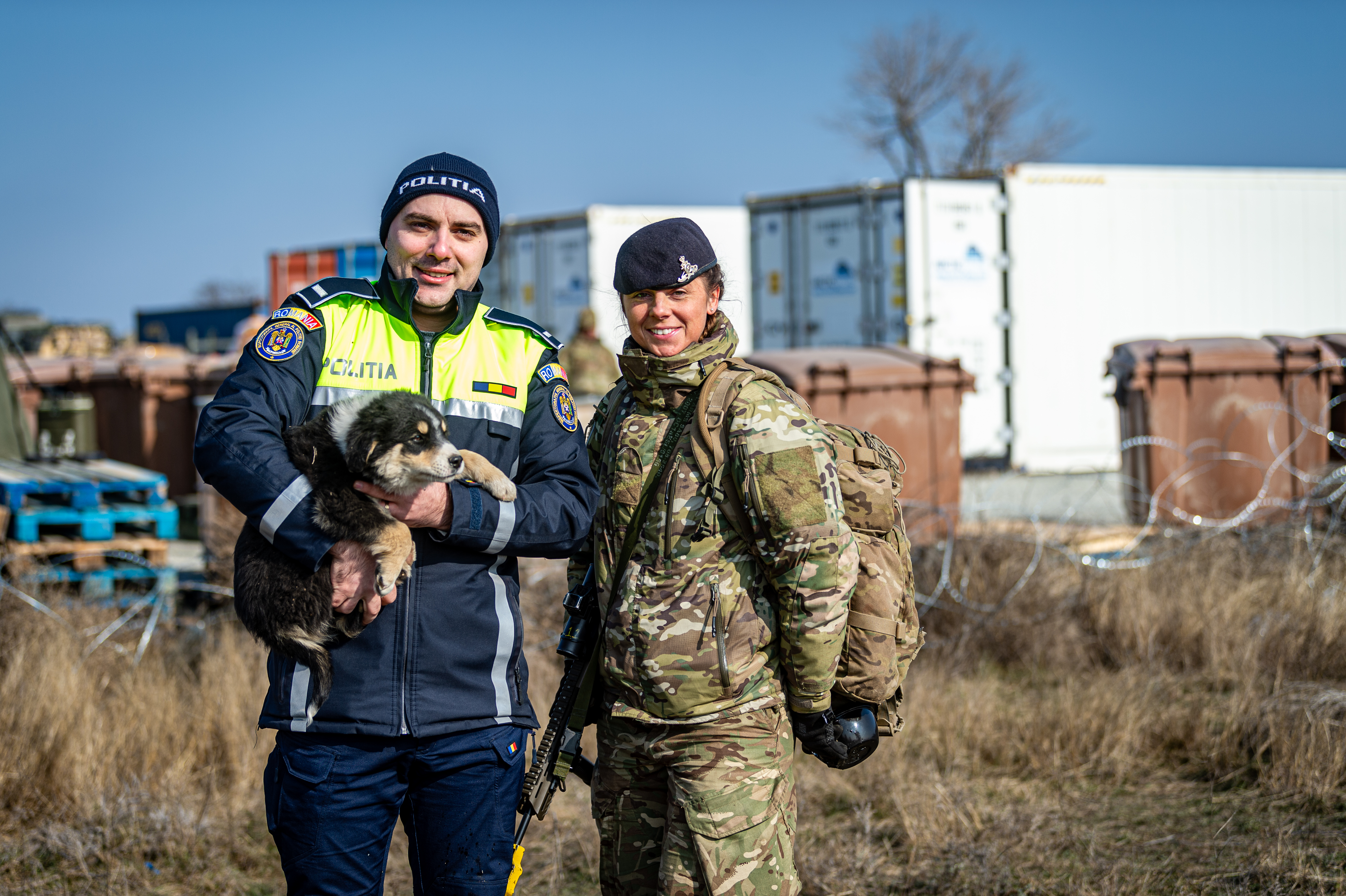 A Romanian police officer holds a puppy whilst standing next to a soldier in uniform.