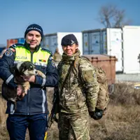 A Romanian police officer holds a puppy whilst standing next to a soldier in uniform.
