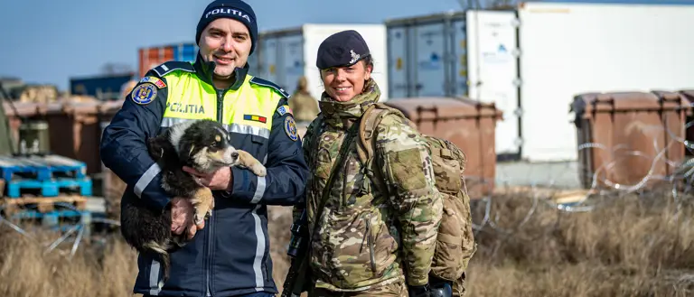 A Romanian police officer holds a puppy whilst standing next to a soldier in uniform.