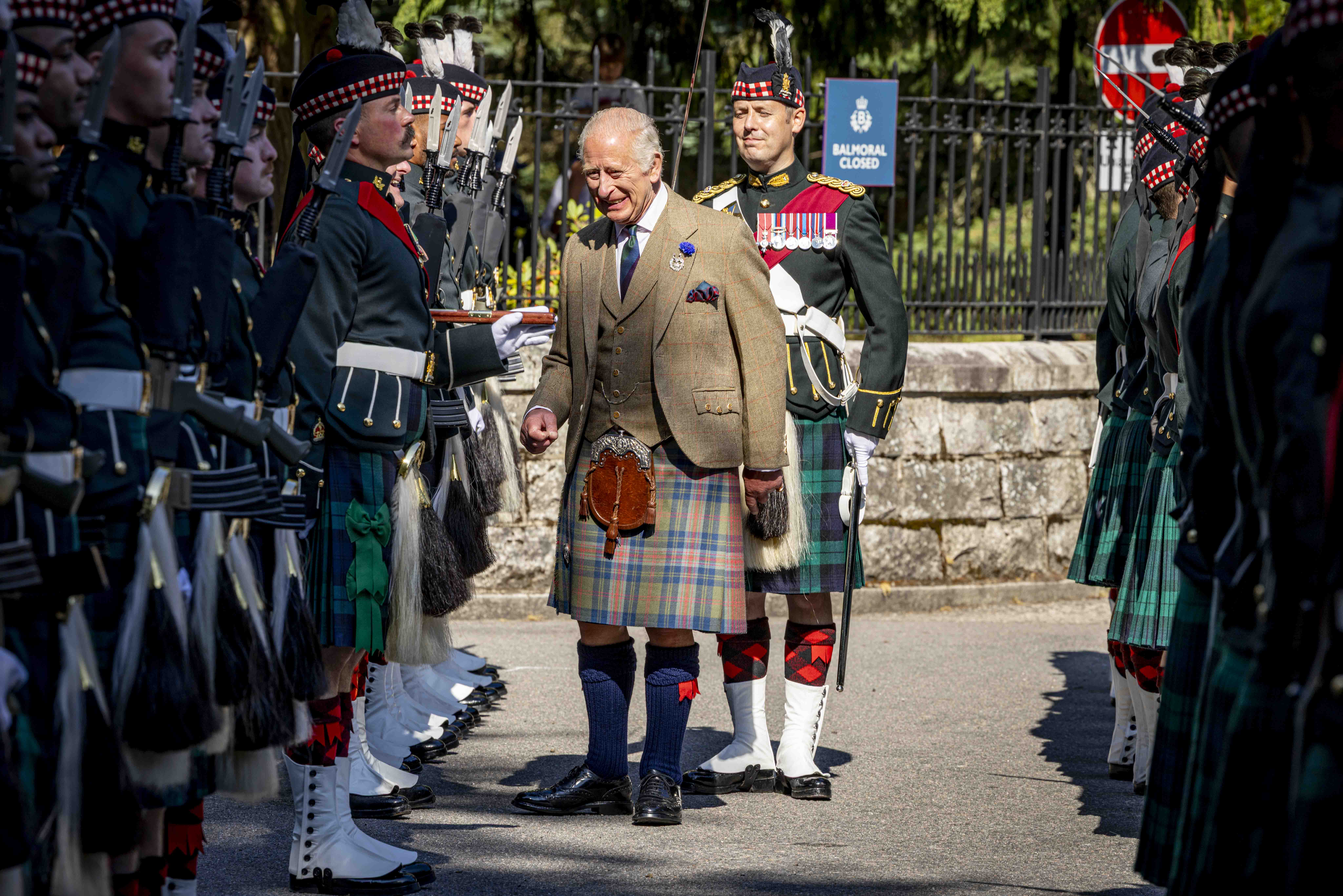  His Majesty The King in a traditional Scottish kilt and tweed jacket inspects soldiers in ceremonial uniform. 