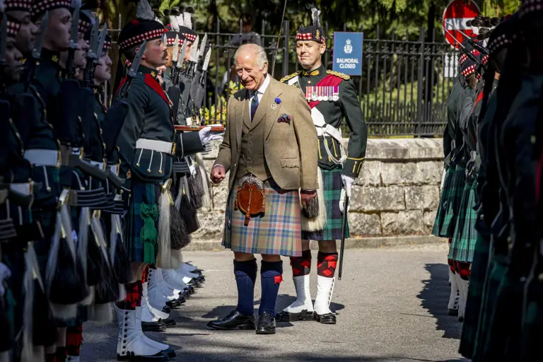  His Majesty The King in a traditional Scottish kilt and tweed jacket inspects soldiers in ceremonial uniform. 