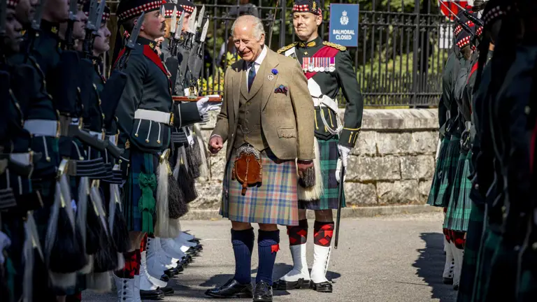 His Majesty The King in a traditional Scottish kilt and tweed jacket inspects soldiers in ceremonial uniform.