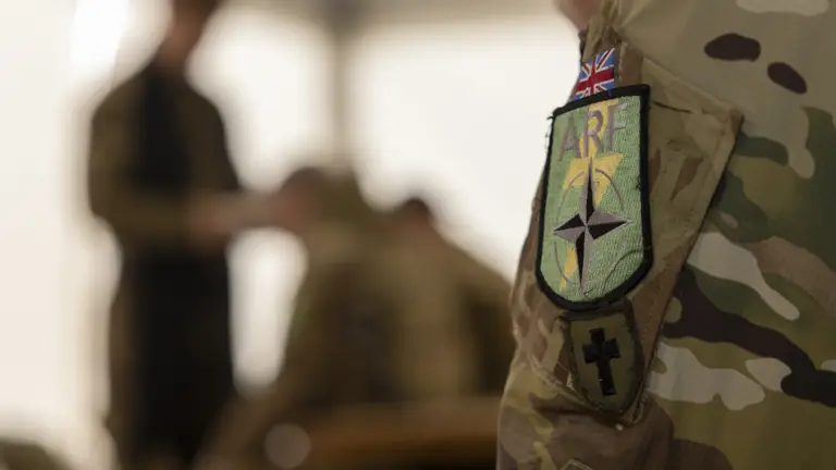 A close up of a British Army padre's shoulder, a British flag, a NATO ARF logo and a crucifix are located on the arm.